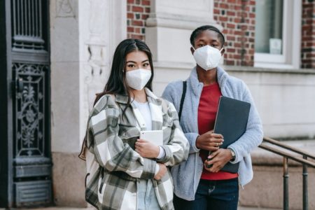 young female teenagers wearing masks while standing on stairs of university